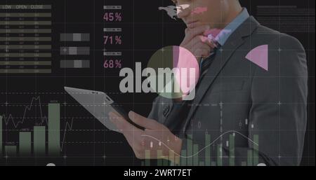 Bild eines jungen kaukasischen Geschäftsmannes, der ein Tablet mit Daten benutzt, die sich im Vordergrund bewegen Stockfoto
