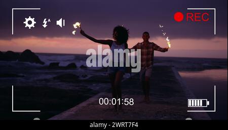 Bild einer jungen Afroamerikanerin und eines jungen, birassischen Mannes am Strand bei Nacht mit Feuerwerk Stockfoto