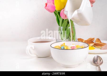 Osterfrühstück Müsli, Cornflakes mit Osterschokoladeneiern und Zuckerstreuseln, Milch oder Joghurt in Cornflakes Golden Breakfast Müsli Portion Stockfoto