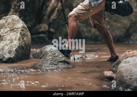 Wanderer nutzen Trekkingstöcke mit Rucksäcken, die durch den Felsen und das Wasser auf dem Bach im Wald laufen. Wander- und Abenteuerkonzept. Stockfoto