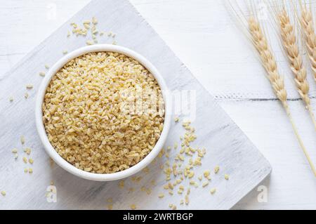 Trocknen Sie Bulgur-Weizenkörner in einer Schüssel oder einem Löffel auf dem Tisch. Haufen von ungekochtem Bulghur, Müsli und Cornflakes Stockfoto