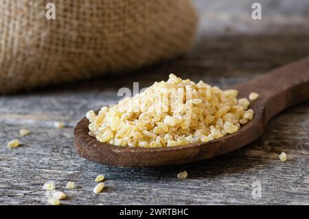 Trocknen Sie Bulgur-Weizenkörner in einer Schüssel oder einem Löffel auf dem Tisch. Haufen von ungekochtem Bulghur, Müsli und Cornflakes Stockfoto