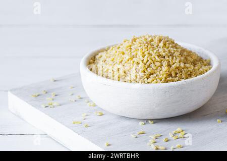 Trocknen Sie Bulgur-Weizenkörner in einer Schüssel oder einem Löffel auf dem Tisch. Haufen von ungekochtem Bulghur, Müsli und Cornflakes Stockfoto