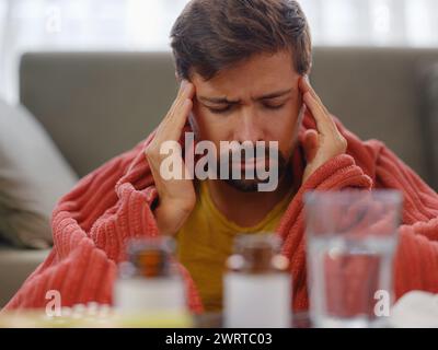 Herbst- und Wintersaison mit Niesen. Junger kaukasischer Mann mit Grippe fühlt sich kalt im Wohnzimmer zu Hause, hat Fieber und Kopfschmerzen und berührt seine Stirn, um seine Temperatur zu überprüfen. Stockfoto
