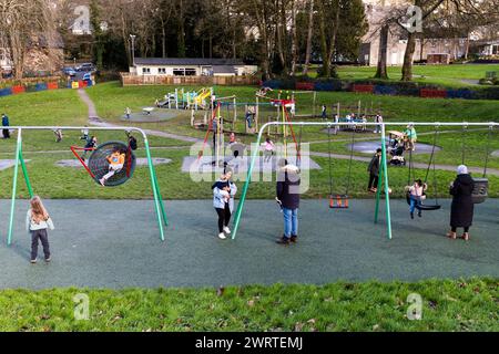 Eltern und Kinder spielen auf Schaukeln auf dem Spielplatz Priory Park in Bodmin Town in Cornwall in Großbritannien. Stockfoto