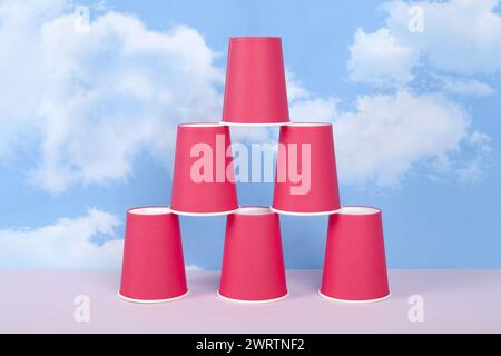 Rote Pappbecher in einer Pyramide, die Erfolg, Gleichgewicht und Stabilität symbolisiert, vor einem blauen Sommerhimmel mit weißen Wolken. Minimaler ph-wert der Stilllebensdauer Stockfoto