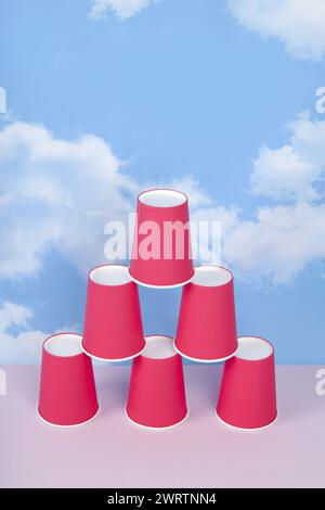 Rote Pappbecher in einer Pyramide, die Erfolg, Gleichgewicht und Stabilität symbolisiert, vor einem blauen Sommerhimmel mit weißen Wolken. Minimaler ph-wert der Stilllebensdauer Stockfoto