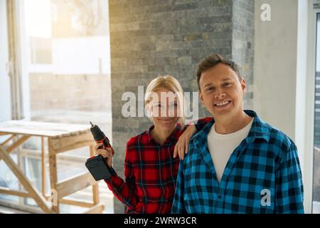 Das Bild von einem lächelnden Mann, der neben einer freudigen Dame steht, die einen elektrischen Schraubenzieher in der erhobenen Hand hält Stockfoto