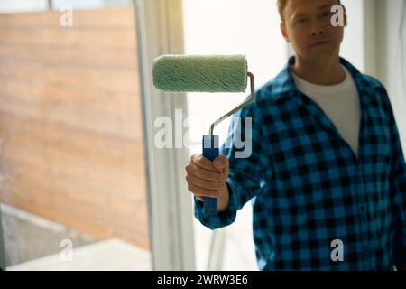 Nahaufnahme eines ernsthaften Arbeiters, der die Malerwalze in der Hand hält Stockfoto