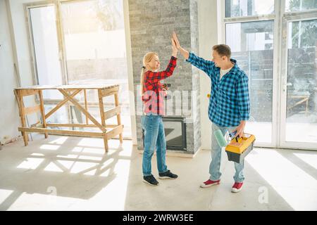 Foto in voller Länge von glücklichem Mann und Frau, die in leerem Raum stehen und einander hohe fünf geben Stockfoto
