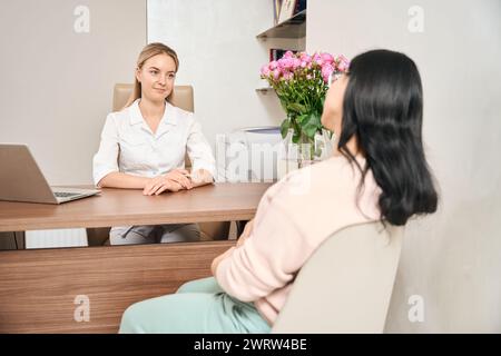 Hübsche junge Frauenärztin, die der schwangeren asiatischen Frau aufmerksam zuhört Stockfoto