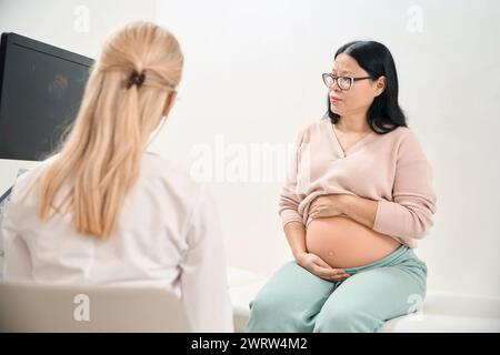 Schwangere Erwachsene Frau beschwert sich über Unwohlsein in ihrem Bauch, fühlt keine Bewegung im Inneren, Ultraschallspezialist überprüft Zustand des Babys in der Motte Stockfoto