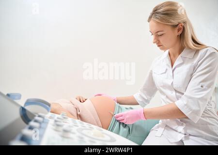 Junger weiblicher Arzt, der schwangere Frau, die auf der medizinischen Liege liegt, Rh-Immunglobulin-Injektionen wegen des Risikos der Rh-Inkompatibilität injiziert Stockfoto