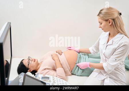 Qualifizierte Krankenschwester, die Injektion an schwangere Frau, die auf medizinischem Behandlungstisch liegt, Impfung, Hormonspiegel Unterstützung, Gesundheit und Medizin Stockfoto