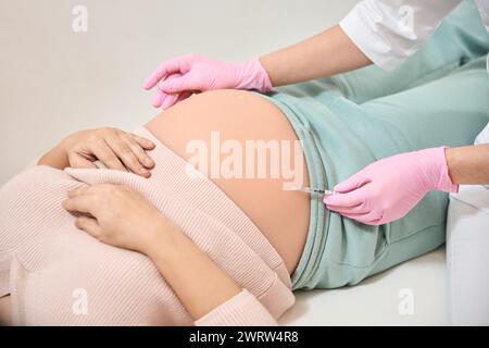 Close-up-Gynäkologe, der Rh-Immunglobulin in den Bauch einer schwangeren Frau injiziert, notwendiges Verfahren wegen Risiko einer Rh-Inkompatibilität Stockfoto