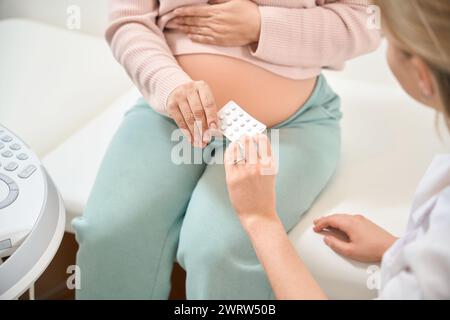 Pflegender Gynäkologe, der schwangere Frauen, die sich über Verstopfung oder Schmerzen in Wirbelsäule und Beinen, Probleme mit Venen wegen beschwert, empfiehlt einige Pillen Stockfoto