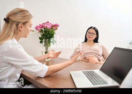 Junge Frau, die mit Schwangeren über Begriffe und Grösse des Babys spricht Stockfoto