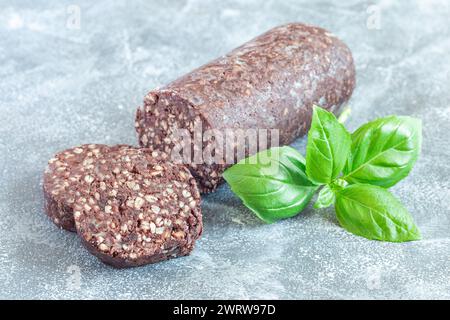 Traditionelle irische und britische Schwarzpudding-Wurstscheiben, Basilikumblätter auf dem Hintergrund, horizontal Stockfoto