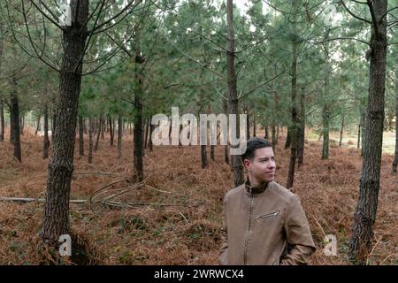 Stockfoto eines attraktiven jungen Mannes mit einer Pelzjacke im Wald, umgeben von Bäumen und trockenen Farnen Stockfoto