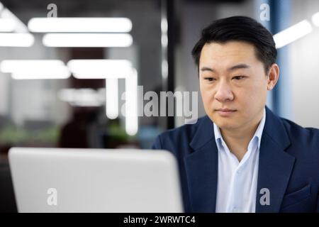 Nahaufnahme eines ernsthaften und fokussierten jungen asiatischen Geschäftsmannes, der im Büro auf einem Laptop arbeitet. Stockfoto