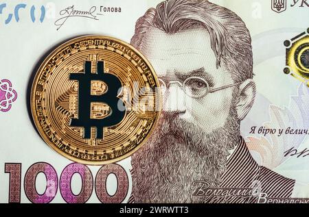 Foto einer goldenen Bitcoin-Münze, die auf einer ukrainischen 1000-Hrivna-Banknote liegt. Stockfoto