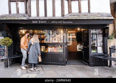 Bristol, Großbritannien. Ein männliches und weibliches Paar halten vor einem Kuchenladen mit Tudor-Fassade oder einer Kuchenfabrik und bewundern die Kuchen, die im Schaufenster zum Verkauf angeboten werden. Stockfoto