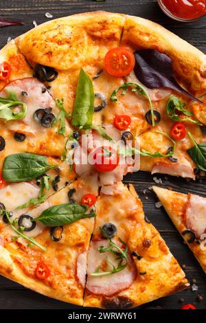 Pizza mit frischem Fleisch, Schinken, Oliven, Käse und Kräutern, Saucen, Olivenöl mit Gewürzen und frischem Gemüse auf dunklem Holzhintergrund. Traditionelles Ital Stockfoto