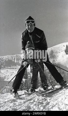 1970er Jahre, historisch, ein Vater mit seinem kleinen Sohn auf einer europäischen Skipiste posierte zusammen für ein Foto. Stockfoto