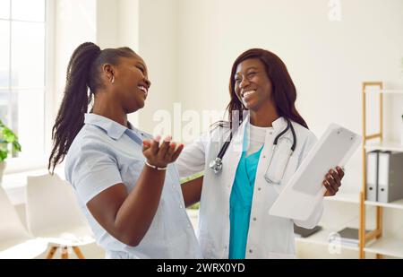 Junge lachende Patientin, die mit ihrem lächelnden Arzt während der ärztlichen Untersuchung in der Klinik spricht. Stockfoto