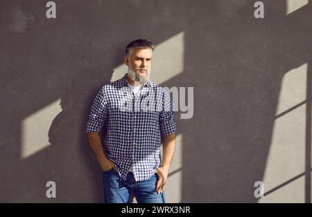 Porträt eines bärtigen Geschäftsmannes mittleren Alters, der an einer grauen Wand steht Stockfoto
