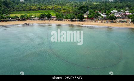 Ein großes Fischernetz schwimmt im Wasser in der Nähe eines belebten Dorfes und eines Sandstrandes in Praia Grande, Sao Tome, Südafrika Stockfoto