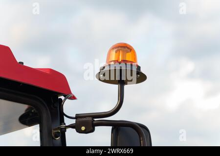 Die orangefarbene Rundumleuchte an der Kabine eines roten Traktors symbolisiert die landwirtschaftliche Sicherheit vor dem Hintergrund eines teilweise bewölkten Traktors Stockfoto