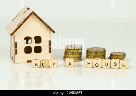 Ein hölzernes Modellhaus neben immer größeren Münzstapeln, mit Blöcken vorne, die das Konzept der Immobilieninvestoren vermitteln Stockfoto