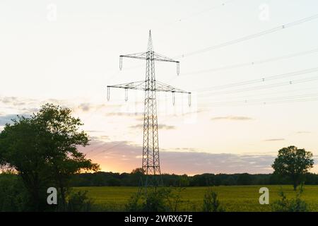 Eine Hochspannungsleitung steht hoch vor einer hellen Sonne im Hintergrund und veranschaulicht die Infrastruktur der Energieübertragung und -Verteilung. Stockfoto