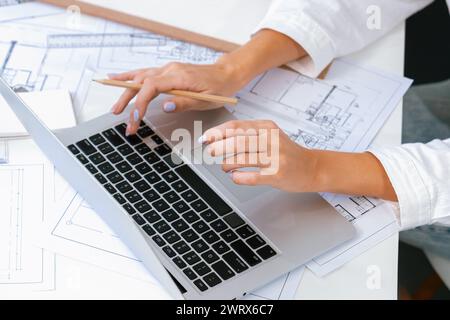 Professioneller, schöner Ingenieur mit Laptop-Analyse-Blueprint mit architektonischem Dokument und Hausmodell auf dem Tisch. Kreatives Business-Design Stockfoto