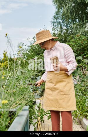 Attraktive, fröhliche, reife Frau mit Strohhut, die ihre Gartenwerkzeuge benutzt und glücklich lächelt Stockfoto