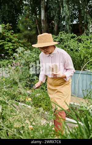 Attraktive, fröhliche, reife Frau mit Strohhut, die ihre Gartenwerkzeuge benutzt und glücklich lächelt Stockfoto