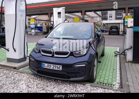 Das BMW i3 Elektroauto wird von einer elektrischen Ladestation, einem Ladekabel, einer weiteren Tankstelle für herkömmliche Benzinautos, die in b zu sehen ist, aufgeladen Stockfoto