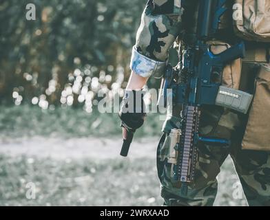 Der Soldat bei der Ausführung von Aufgaben in Tarnhülle und Schutzhandschuhen mit einer Waffe. Kriegsgebiet. Stockfoto