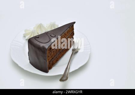 Stück Sachertorte mit Schlagsahne auf weißem Teller, Nahaufnahme, isoliert auf weißem Hintergrund Stockfoto