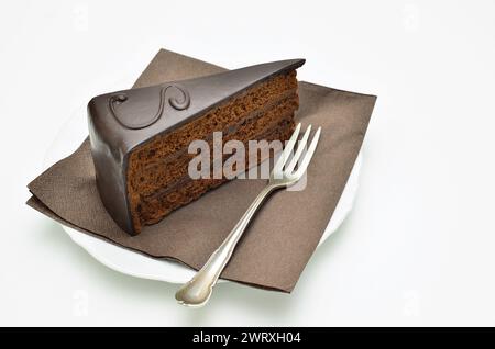 Stück Sacher-Torte auf weißem Teller, mit Gabel und brauner Serviette, isoliert auf weißem Hintergrund Stockfoto