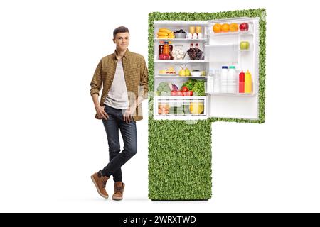 Der Kerl lehnt sich auf einen grünen, nachhaltigen Kühlschrank, isoliert auf weißem Hintergrund Stockfoto