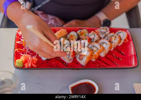 Eine Nahaufnahme weiblicher Hände mit Stäbchen, um Sushi von einem Teller in einem Restaurant zu holen. Curacao. Stockfoto