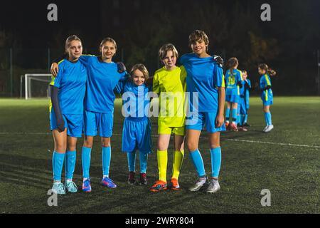 Mitglieder der Schulmädchen-Fußballmannschaft machen gemeinsam ein Foto in einem Stadion beim Abendtraining, Vollaufnahme, Teamunterstützung. Hochwertige Fotos Stockfoto