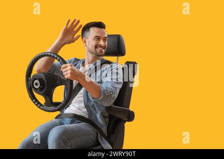 Gutaussehender Mann mit dem Lenkrad, der Hand im Autositz auf gelbem Hintergrund winkt Stockfoto