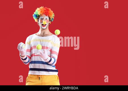 Porträt von Clown, der Tennisbälle jongliert auf rotem Hintergrund. Aprilfeier zum Narrentag Stockfoto