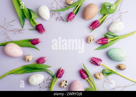 Kreisförmiges Layout mit Ostereiern, Tulpenblüten auf pastellfarbenem Fliederhintergrund. Draufsicht, flach, Kopierbereich. Stockfoto