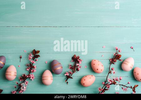 Osterflachlage mit bemalten Eiern, Kirschblüten und Blütenblättern auf türkisblauem Hintergrund. Draufsicht, Kopierraum. Stockfoto