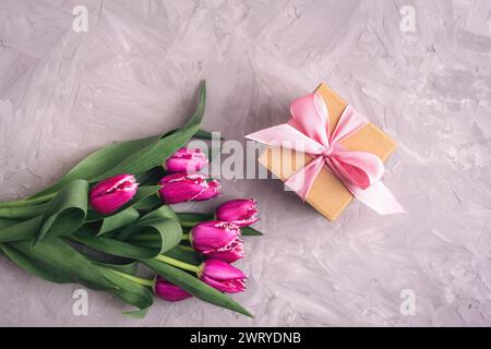 Pinkfarbene Tulpen und Geschenk in einer Schachtel auf grauem, strukturiertem Tisch. Frühling festlicher Hintergrund, Draufsicht, flache Lay. Stockfoto