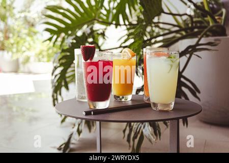 Ein Tisch mit fünf verschiedenfarbigen Getränken und einer grünen Pflanze im Hintergrund. Die Getränke sind in hohen Gläsern. Stockfoto